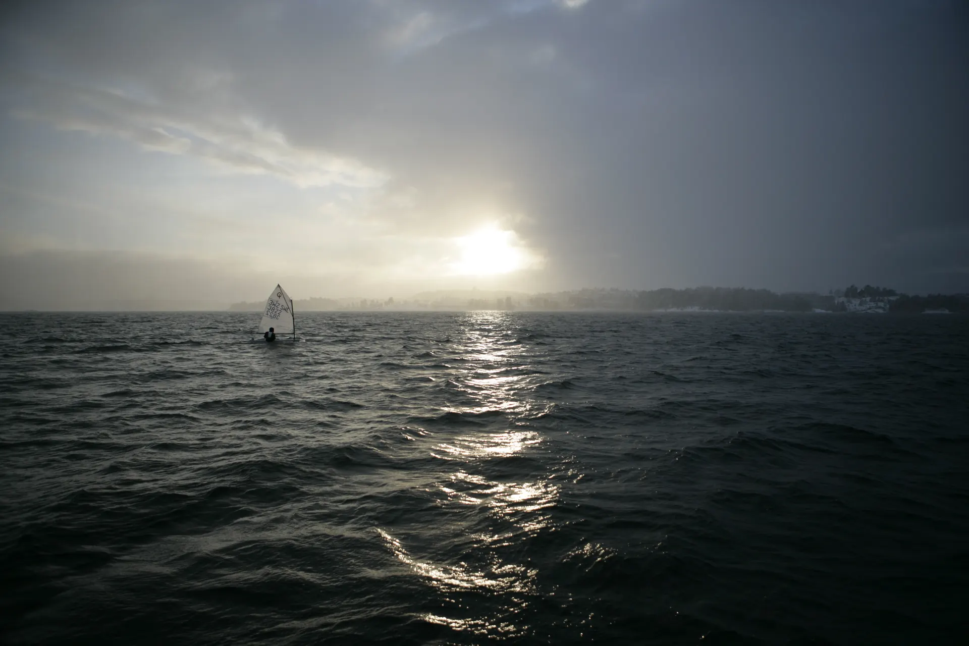 A lone Optimist sailing under a storm sky